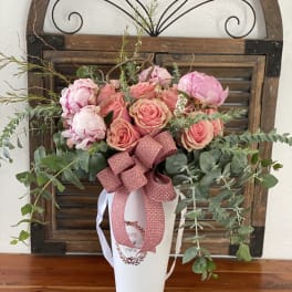 Pink roses and peonies arranged in a white vase with a ribbon