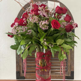 Red roses and pink filler flowers in a tall glass vase with ribbon