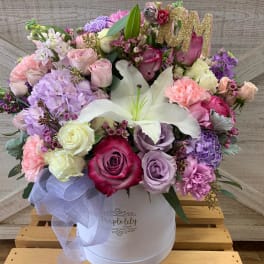 Pastel bouquet of roses, lilies, and carnations in a white hat box with a glittery "M" topper