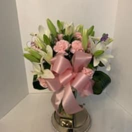 Pink and white flower arrangement with a large satin bow in a metal vase