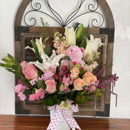 Pink and white floral arrangement with a teddy bear in a white vase