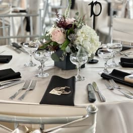 Round table centerpiece with pale pink and white flowers in a black vase
