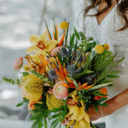 Bride holding a colorful tropical bouquet with yellow orchids and orange blooms