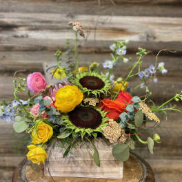Mixed bouquet in a wooden box with sunflowers, roses, and blue flowers