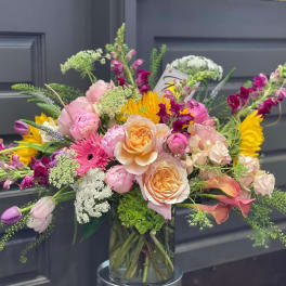 Mixed bouquet of pink, peach, and yellow flowers in a glass vase