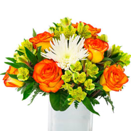 Compact orange and yellow roses with green flowers and a white bloom in a clear glass cube vase