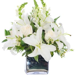 White lilies, roses, and snapdragons arranged in a silver cube vase