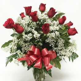 Dozen red roses with white filler flowers in a glass vase with a red ribbon bow
