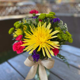 Bouquet of yellow, pink, green, and purple flowers tied with a beige ribbon
