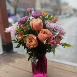 Bouquet of peach roses and purple flowers in a pink glass vase