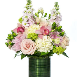 Arrangement of soft pink roses, orchids, and white hydrangeas in a green cylinder vase