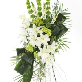 Tall white and green standing spray with lilies, snapdragons, and bold tropical leaves on a metal easel.