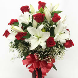 Tall arrangement of red roses and white lilies in a red vase with a bow
