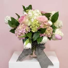 Pink and white roses, hydrangeas, and tulips in a glass vase with a striped ribbon
