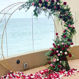 Floral arch with red, pink, and white roses over a petal-covered floor