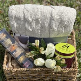Gift basket with white roses, chocolates, and a folded knit throw