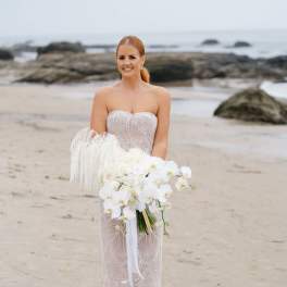 Bride holding a white orchid bouquet on a beach