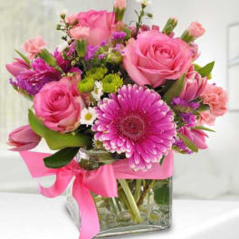 Pink roses and gerbera daisies in a glass vase with a pink ribbon