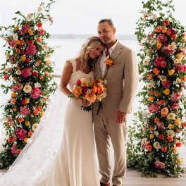 Bride and groom with colorful floral wedding arch and bouquet