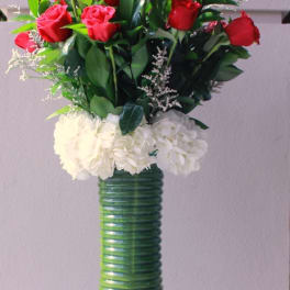 Red roses arranged in a tall green vase with white flowers at the base