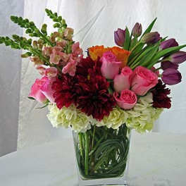 Mixed bouquet of pink roses, tulips, and burgundy blooms in a glass vase