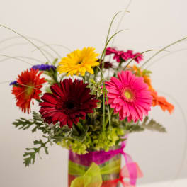 Colorful gerbera daisy arrangement in a square glass vase with ribbon