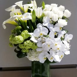 White calla lilies, roses, and orchids in a tall glass vase