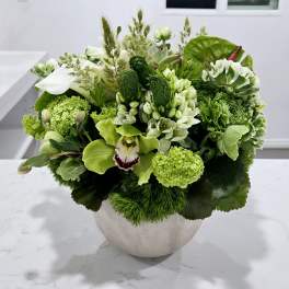 Green floral arrangement in a round white vase with white and lime blooms