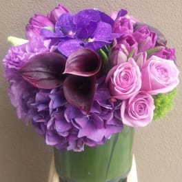 Purple bouquet with roses, hydrangea, calla lilies, and orchids in a glass vase