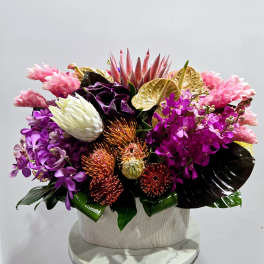 Tropical floral arrangement with pink, purple, and gold blooms in a white vase