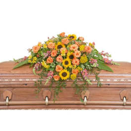 Bright casket spray with sunflowers and orange roses on a wooden casket