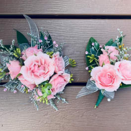Two pink rose boutonnieres with silver ribbon and greenery