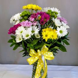 Mixed daisy bouquet in a glass vase with a yellow polka-dot ribbon
