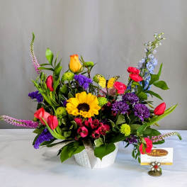 Colorful mixed flower arrangement in a white basket with a butterfly pick