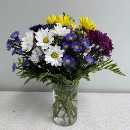 Mixed bouquet of daisies and purple flowers in a clear glass vase