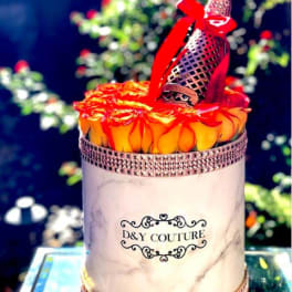 Round box of orange roses with a decorative bottle on top