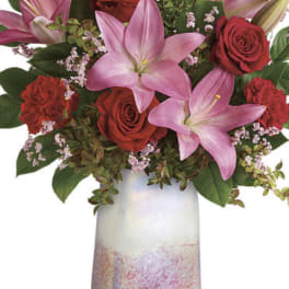 Pink lilies and red roses arranged in a tall iridescent vase