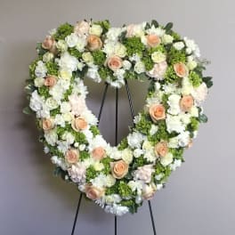 Heart-shaped floral wreath on a stand with white and peach flowers