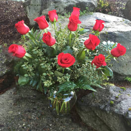 Red roses arranged in a clear glass vase with mixed greenery