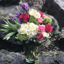 Bouquet of roses, hydrangeas, and purple flowers in a glass vase
