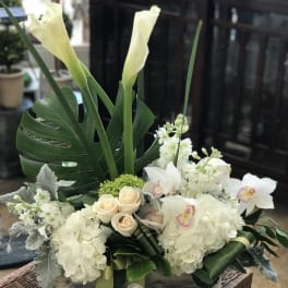 White floral arrangement with calla lilies, roses, and orchids in a wooden box