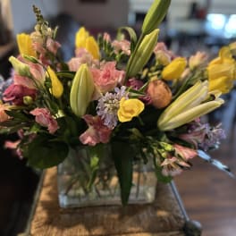 Mixed bouquet with yellow lilies, pink blooms, and a glass vase