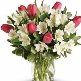 Pink tulips and white flowers arranged in a clear glass vase