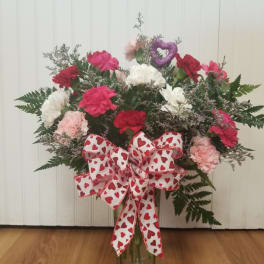 Heart-themed bouquet of pink, red, and white carnations in a glass vase