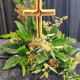 Cross-shaped floral tribute with mixed greenery and small pale blooms