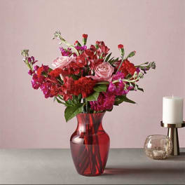 Red and pink bouquet in a red glass vase beside a candle