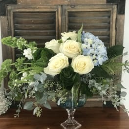 Cream roses and blue hydrangea in a glass pedestal vase