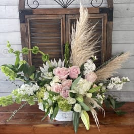Arrangement of pink and white flowers in a white container with pampas grass
