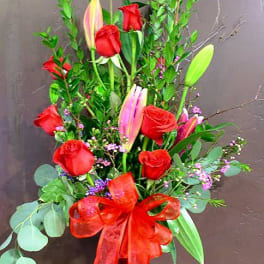 Tall bouquet of red roses and pink lilies in a glass vase with a red ribbon
