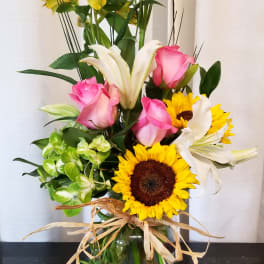 Mixed bouquet with pink roses, sunflowers, white lilies, and yellow alstroemeria in a glass vase